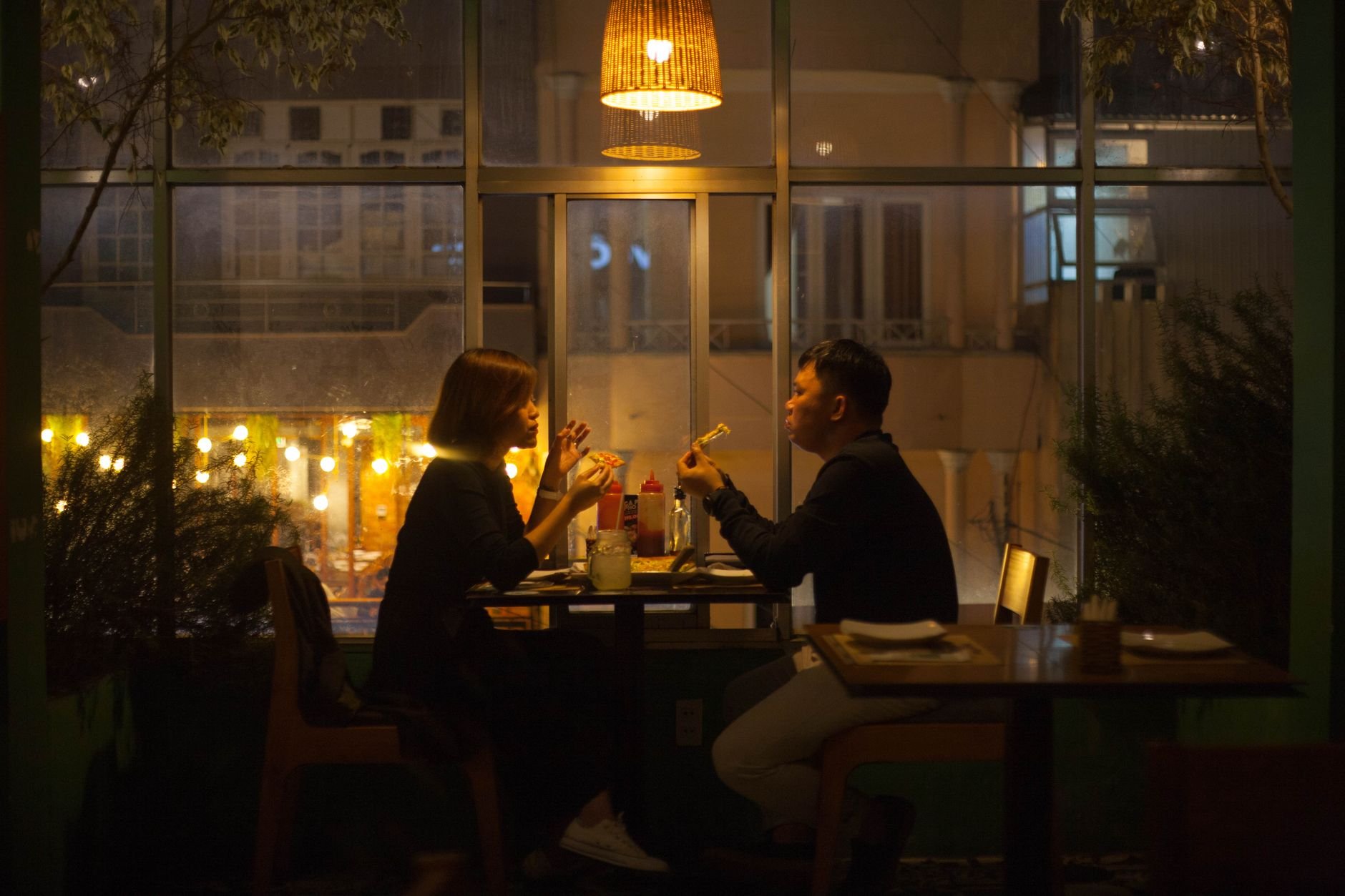 A couple enjoys a candlelit dinner in a warm, cozy restaurant interior at night.